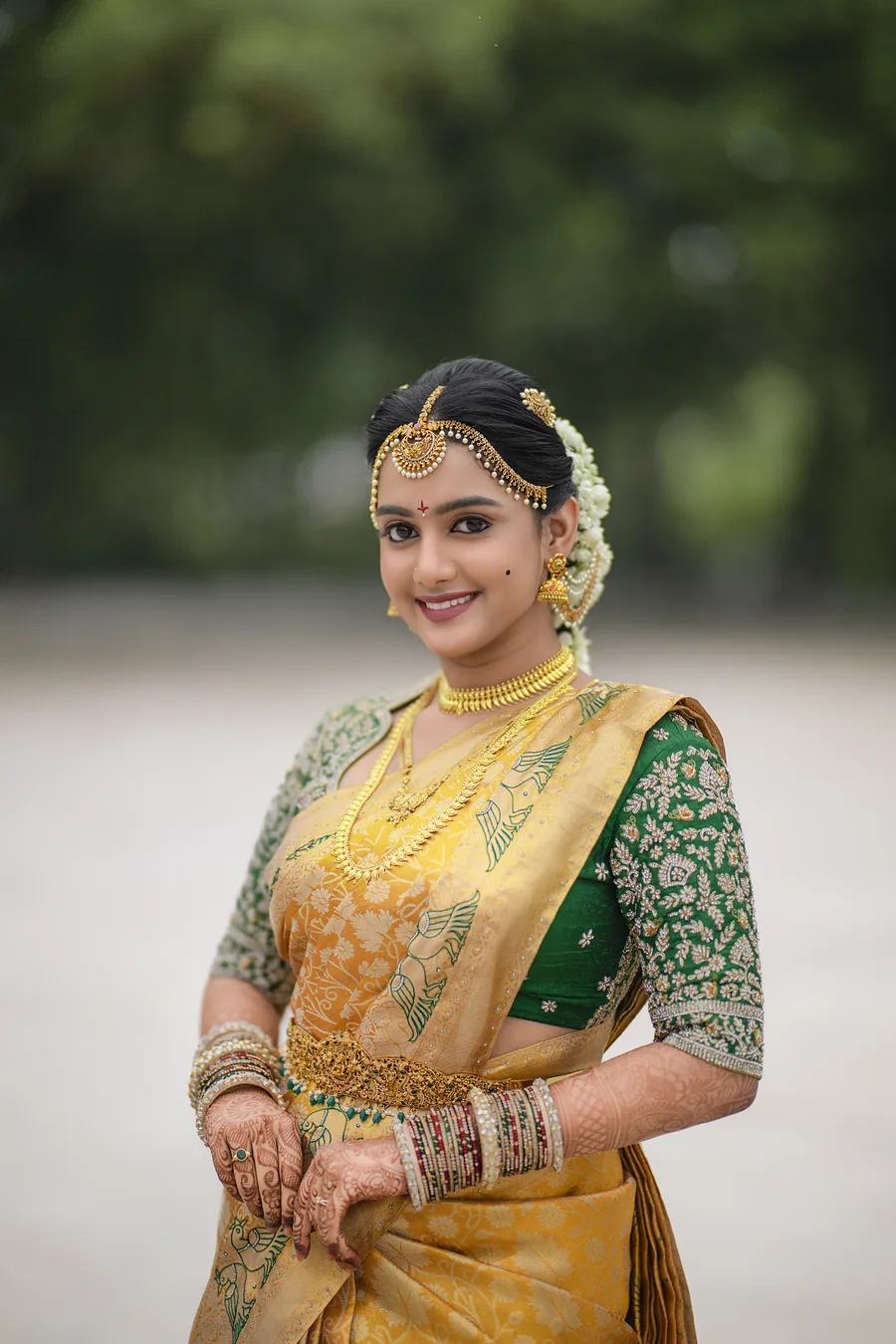 Harini Veena smiling in a mustard and green Kanjivaram silk saree with temple jewellery