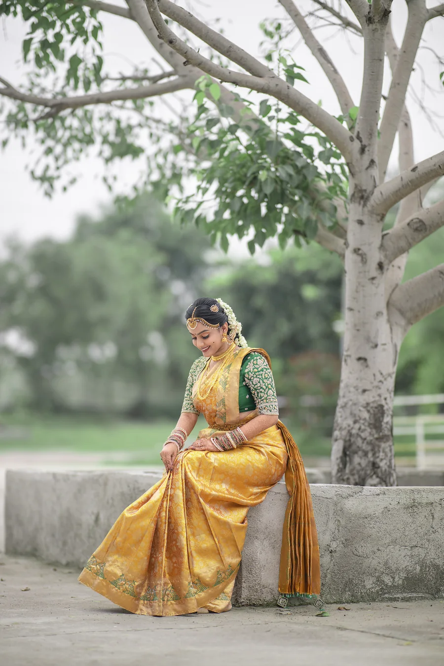 Harini Veena seated under a tree in a mustard Kanjivaram silk saree