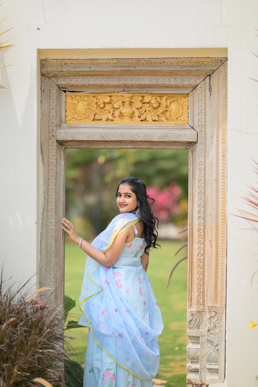 Harini Veena in a pastel blue organza outfit framed by a carved wooden doorway