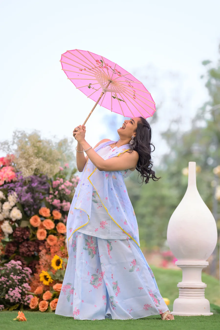Harini Veena twirling a pink paper parasol in a pastel blue floral outfit