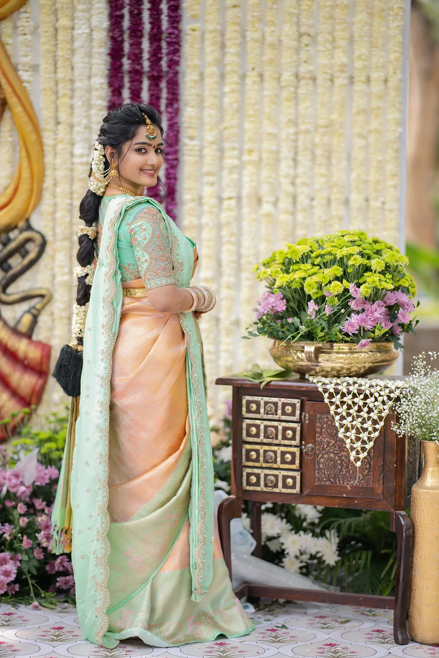 Harini Veena in a peach and mint silk saree with a jasmine braid, standing beside a flower-filled table