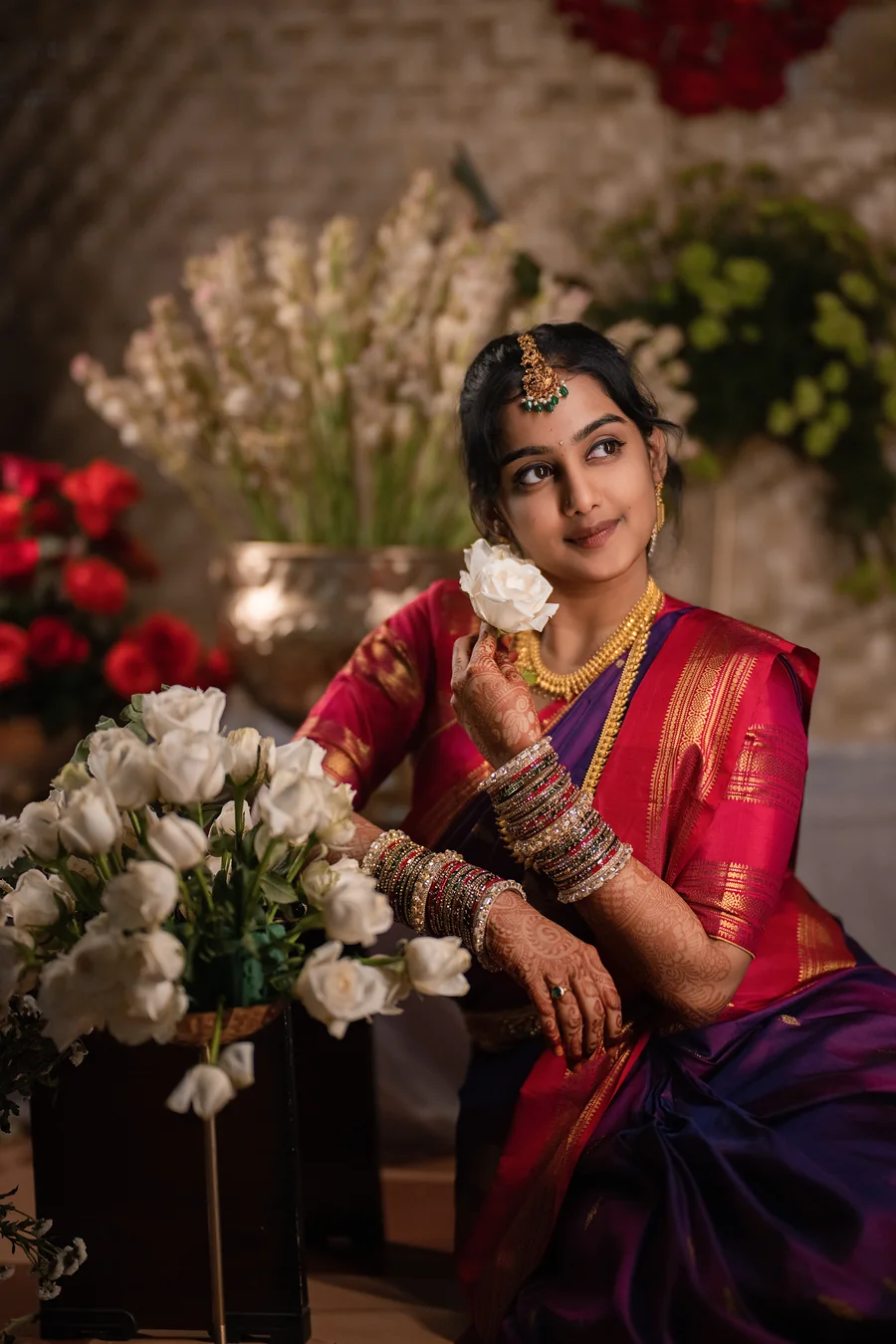 Harini Veena in a magenta and purple silk saree with temple gold jewellery, holding a white rose