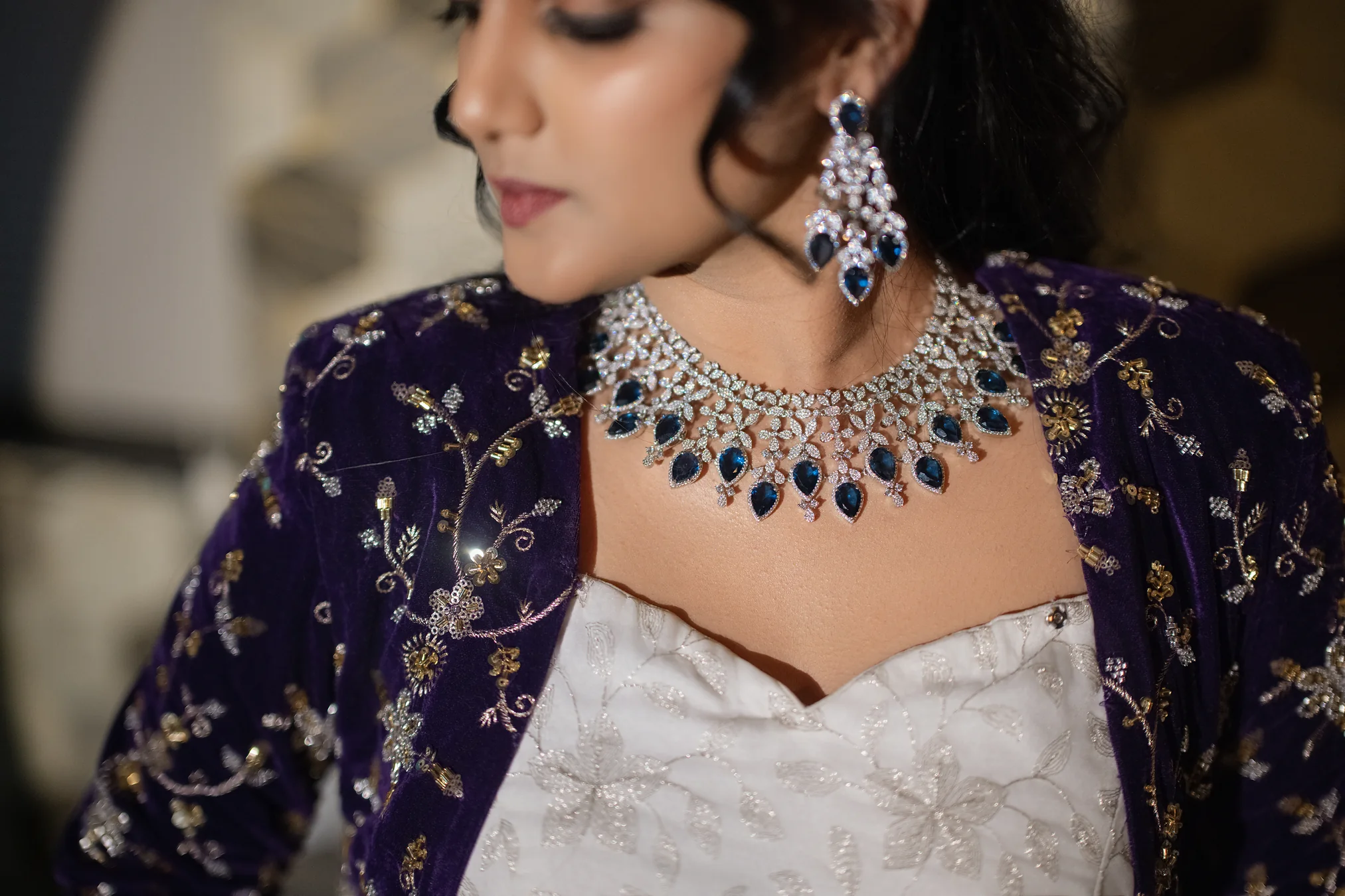 Close-up of a diamond and sapphire necklace and earrings with a purple velvet jacket