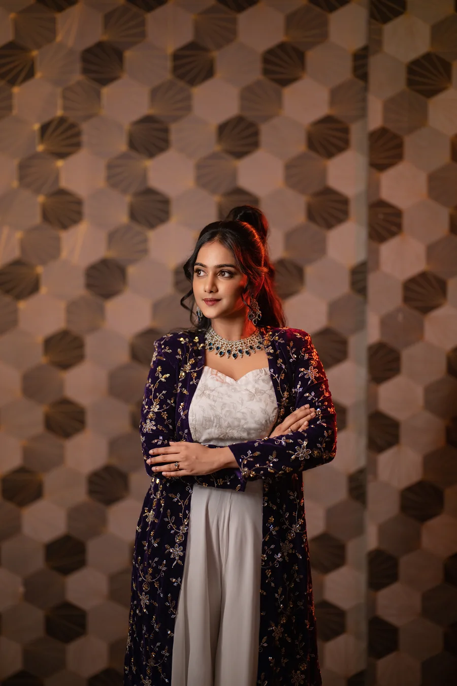 Harini Veena in a purple velvet jacket and white outfit against a hexagon wall